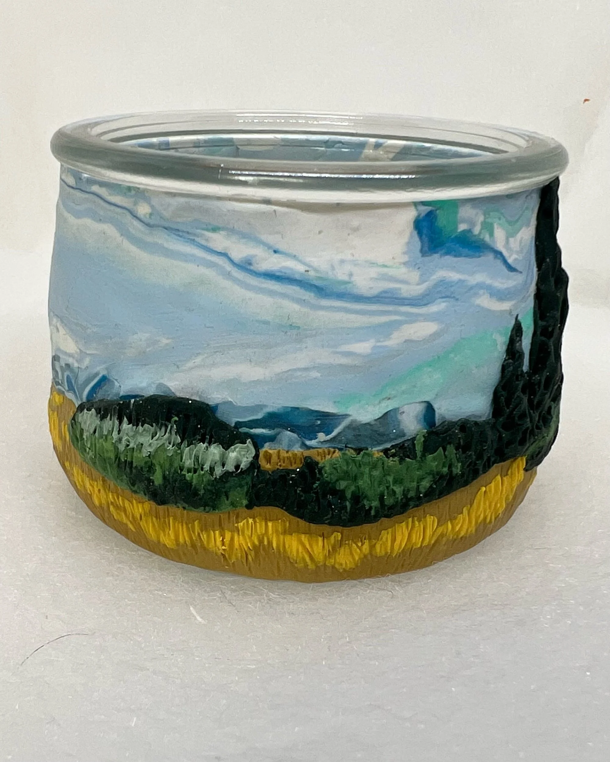 A round glass container with a painted landscape scene featuring mountains, sky, and green and yellow fields.