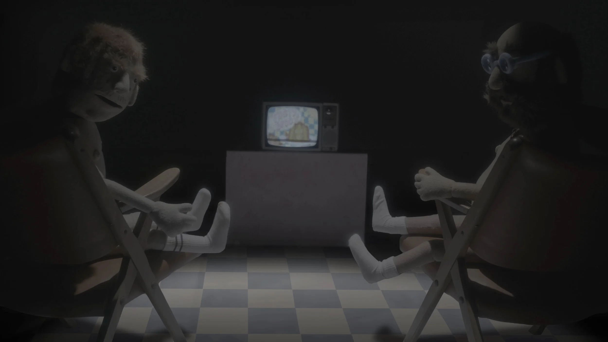 Two sock puppet characters with glasses sitting in chairs in a dark room, watching a small television on a stand, with the TV screen showing a pixelated scene.