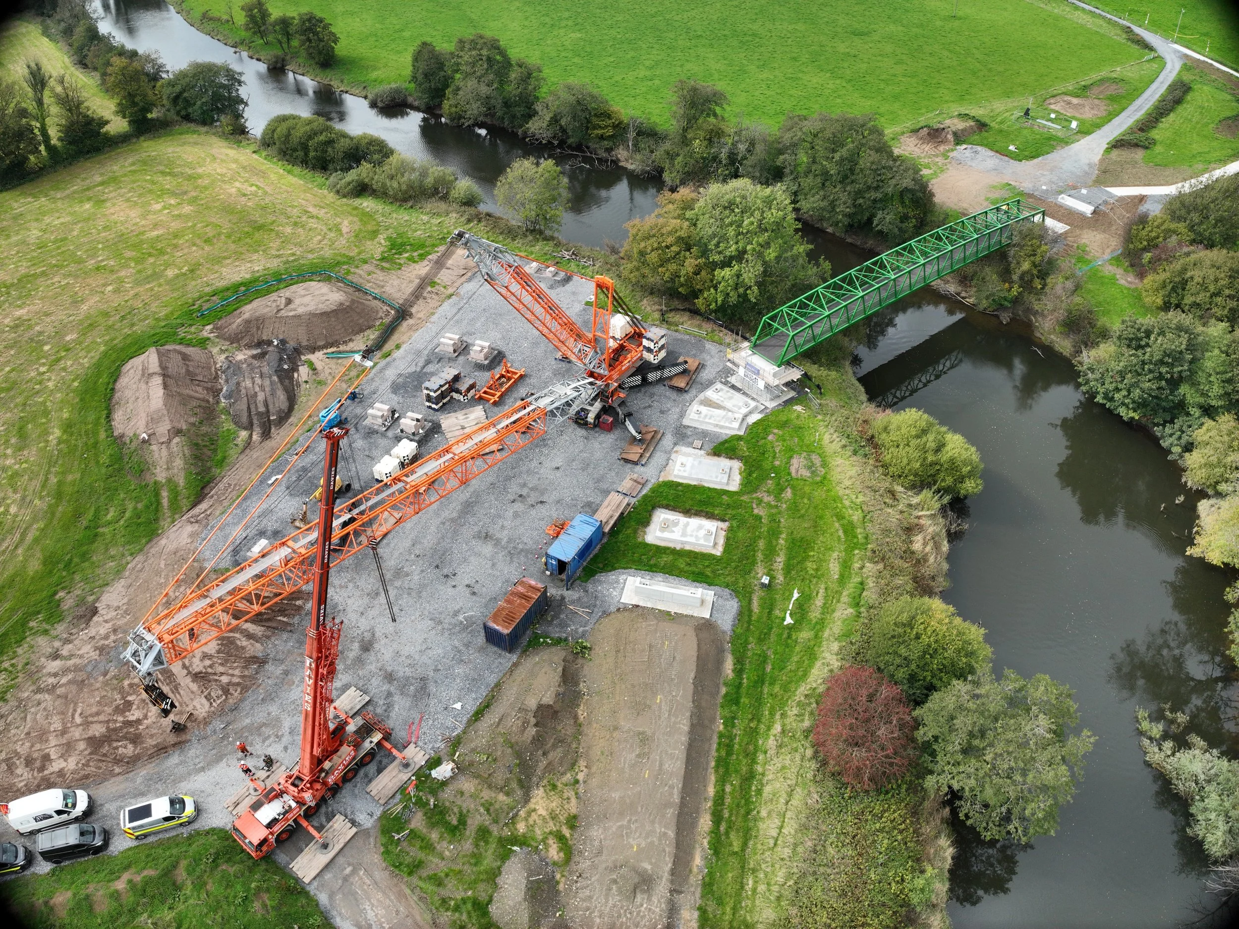 Aerial view of construction site with cranes next to a river, building a bridge.