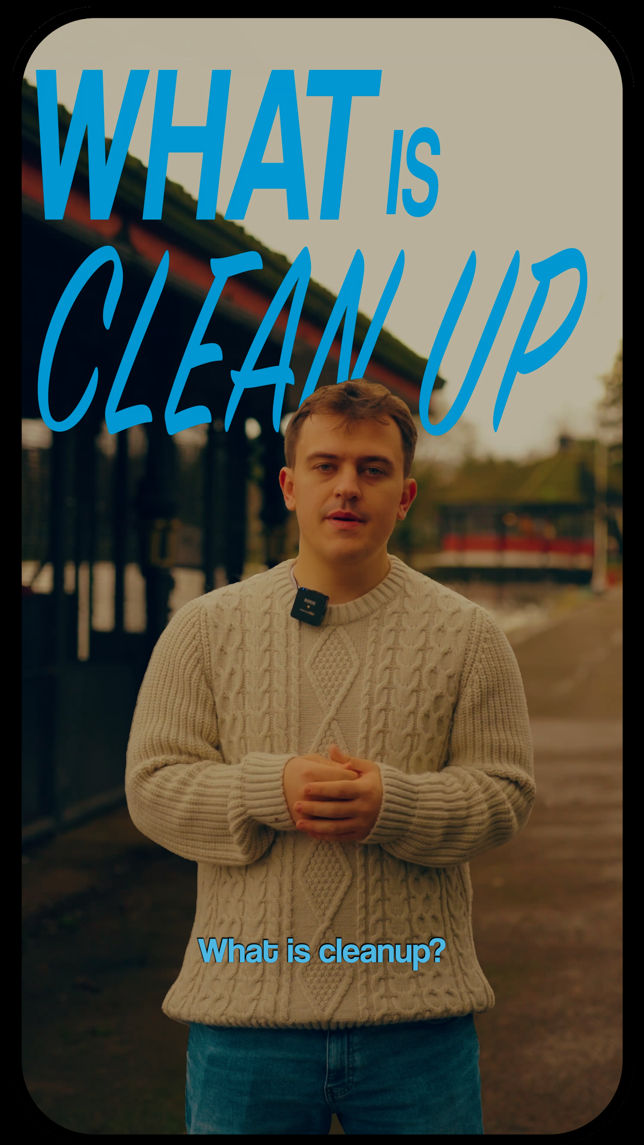 A young man in a cream-colored knit sweater stands outdoors near a fence and a train station, holding his hands together, with the text "What is clean up" and "What is cleanup?" overlaid on the image.
