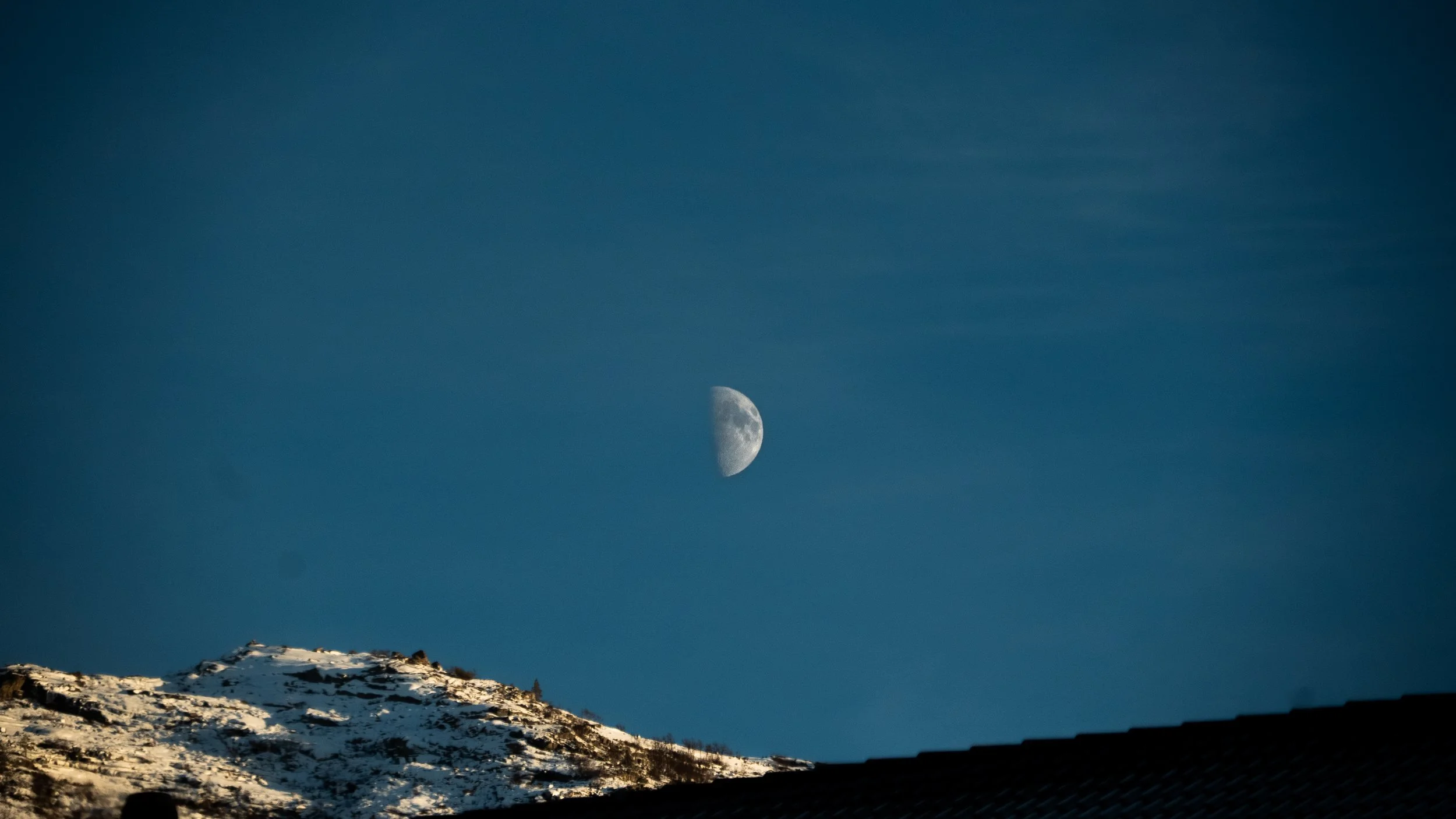 Night sky with a visible moon over snowy mountain landscape.