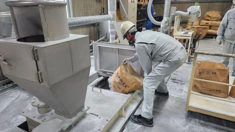 A man in a hard hat and overalls emptying material into a machine
