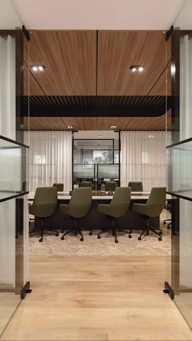 Commercial office interior featuring custom glass walls, a large marble conference desk, and integrated wood shelving with warm accent lighting.