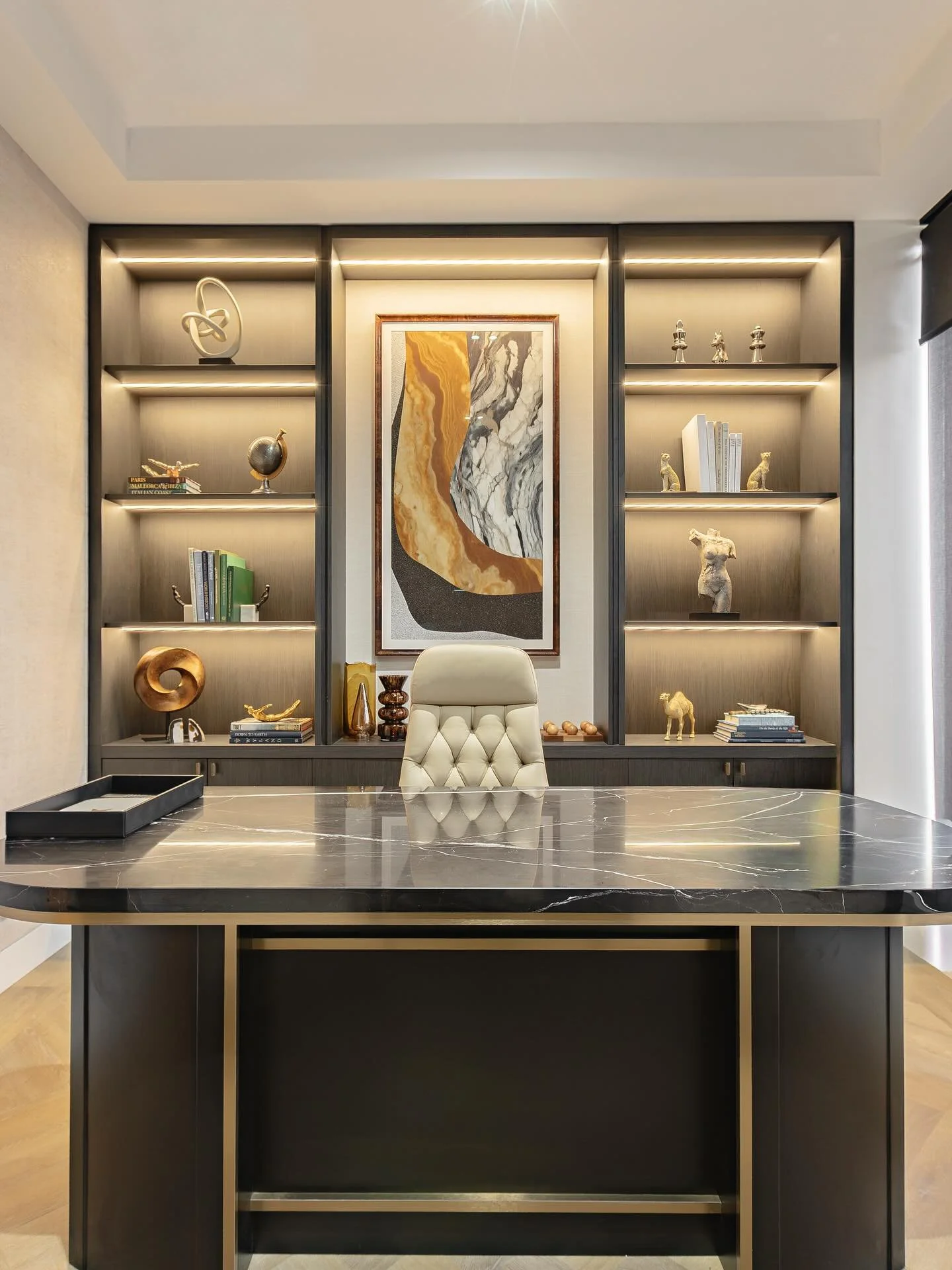 Commercial office interior featuring custom glass walls, a large marble conference desk, and integrated wood shelving with warm accent lighting.