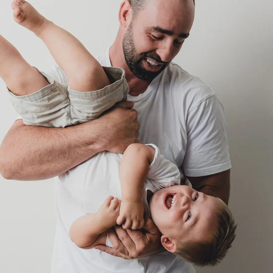 A man playing with a young boy, lifting him up and smiling.