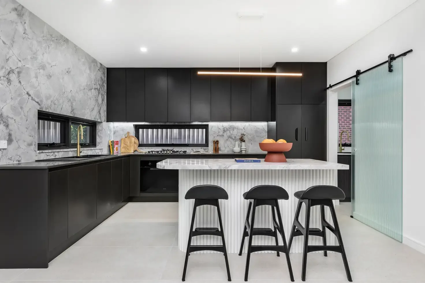 Modern kitchen featuring matte black cabinetry, marble island, and a custom fluted glass barn door with black hardware