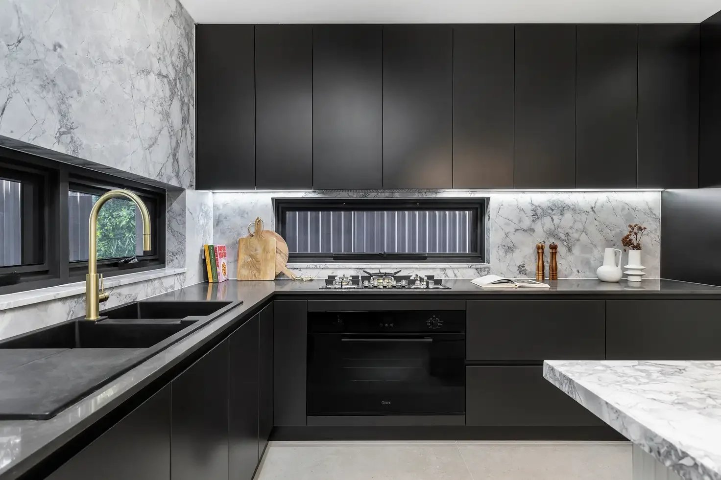 Modern kitchen featuring matte black cabinetry, marble island, and a custom fluted glass barn door with black hardware