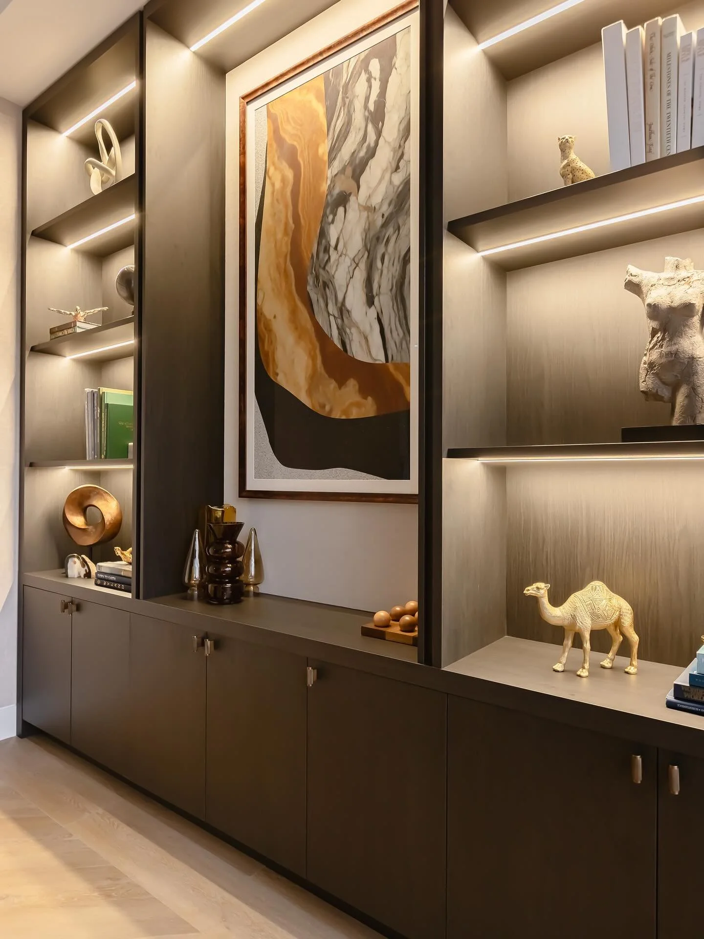 Commercial office interior featuring custom glass walls, a large marble conference desk, and integrated wood shelving with warm accent lighting.
