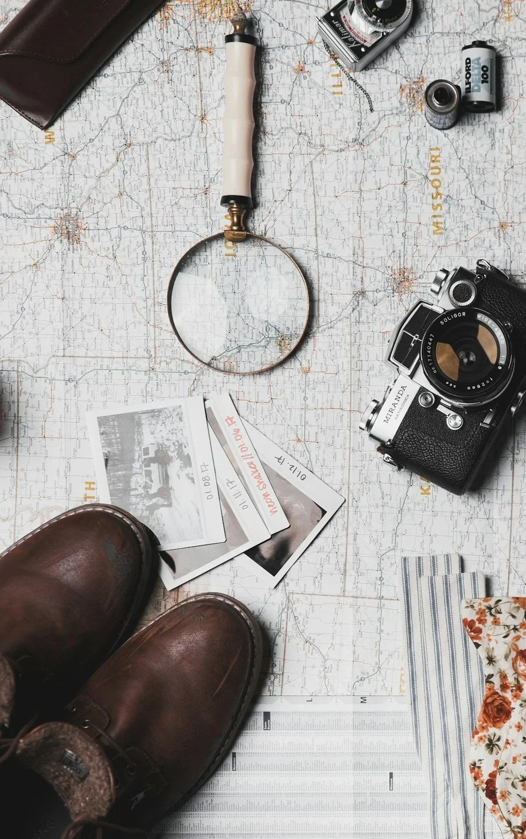 Travel planning setup with boots, Polaroid photos, vintage camera, a magnifying glass, flashlight, and a map of Missouri.