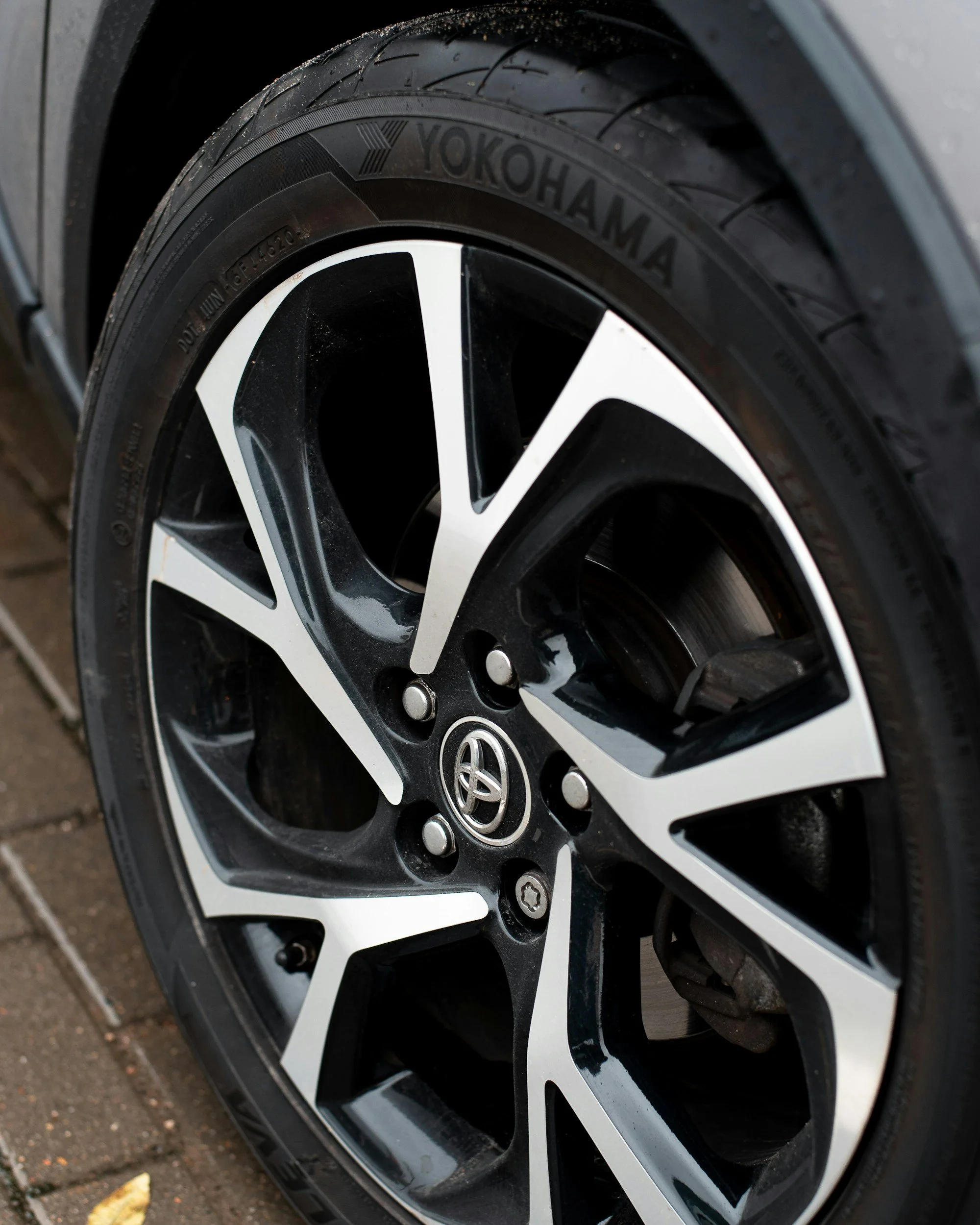 Close-up of a car tire and alloy wheel with a Toyota logo, mounted on a wet road surface.