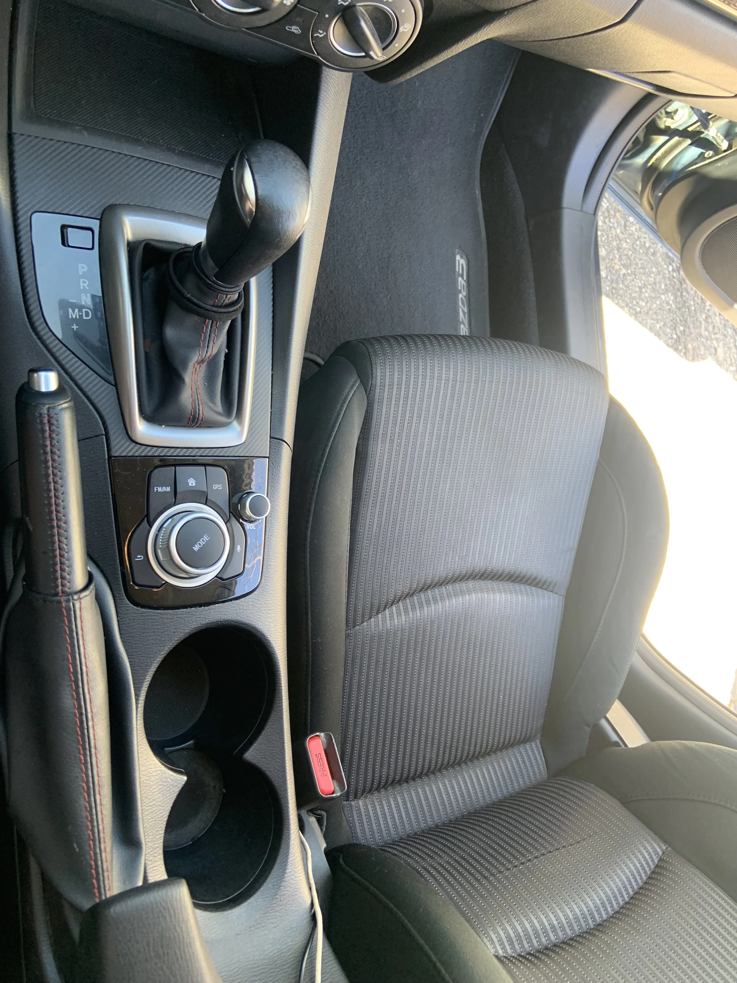 Interior of a car showing the gear shift, control knobs, cup holders, and front passenger seat.