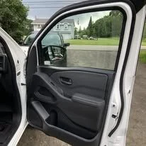 Open car door showing the interior door panel and side mirror with a green grassy area and trees in the background.