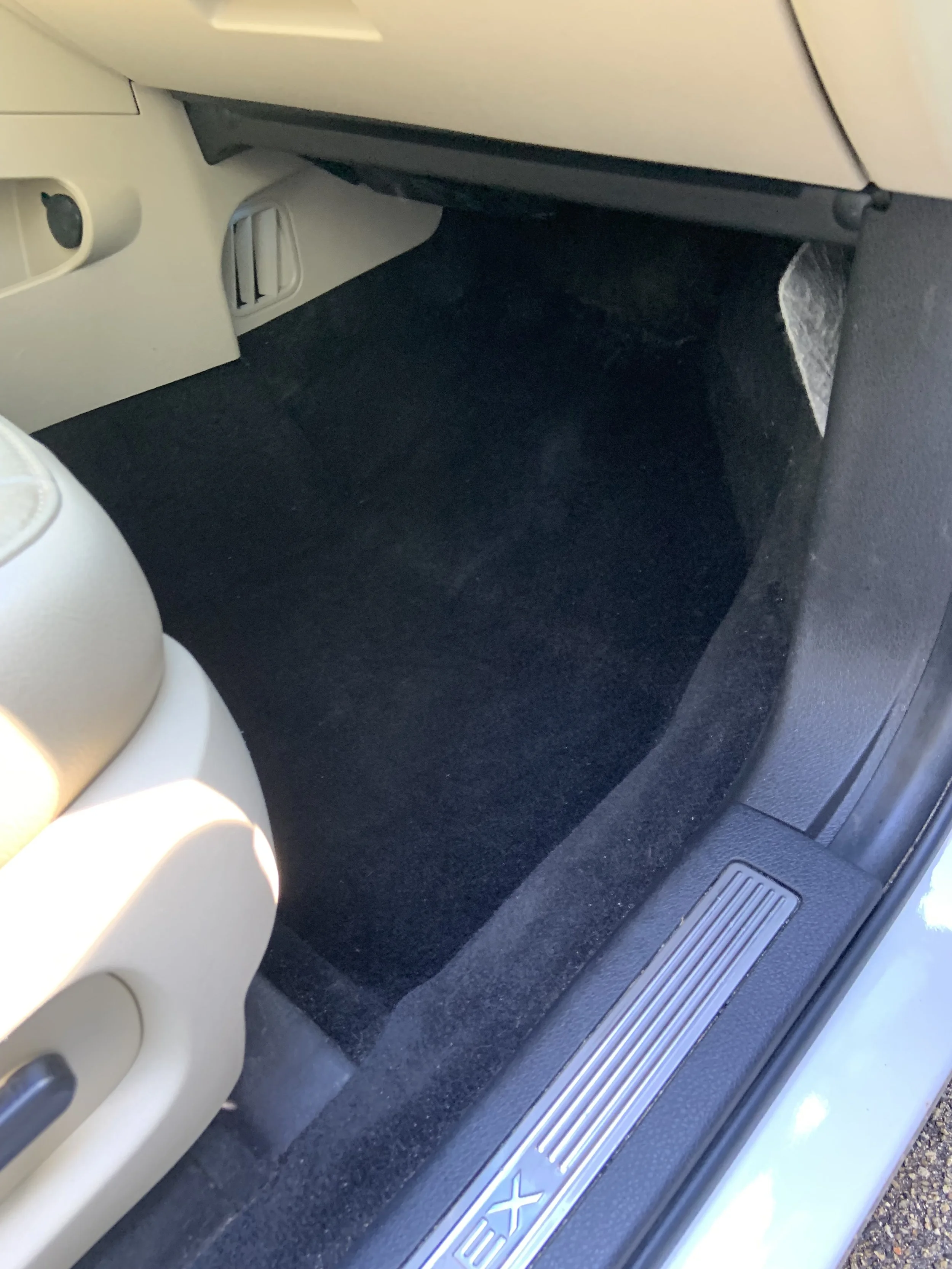Car interior showing the beige passenger seat, black carpeted floor, and a metal door sill with the logo 'EX'.