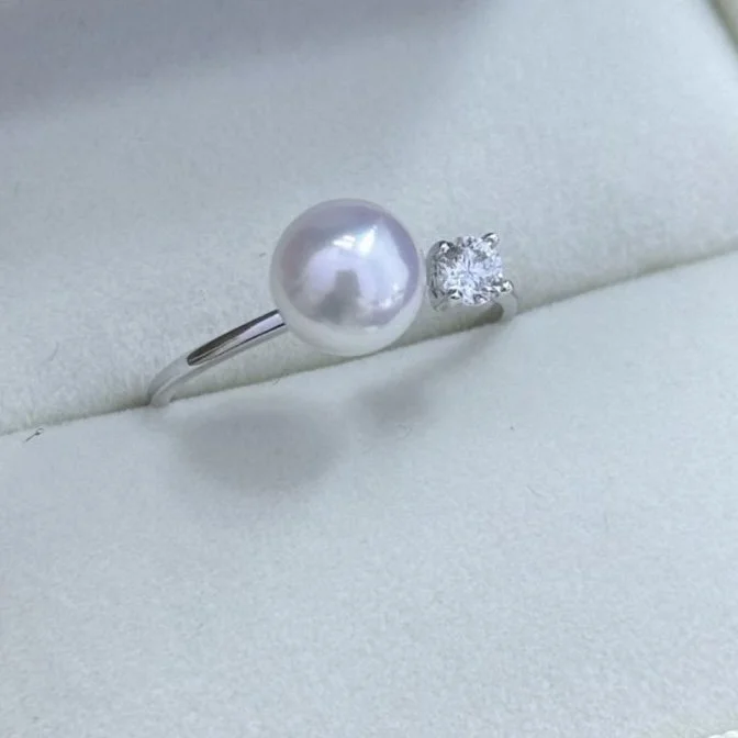 A silver ring with a large pearl on one side and a small square cut rhinestone on the other, resting on a light-colored surface.