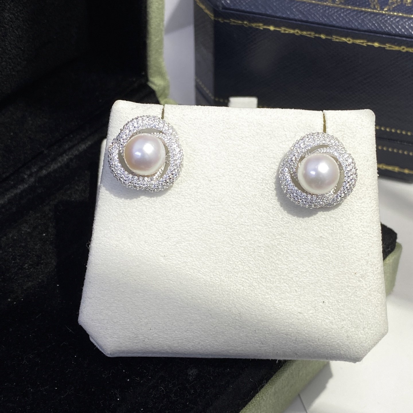 Pair of pearl earrings with surrounding small diamonds on display in a white jewelry stand.