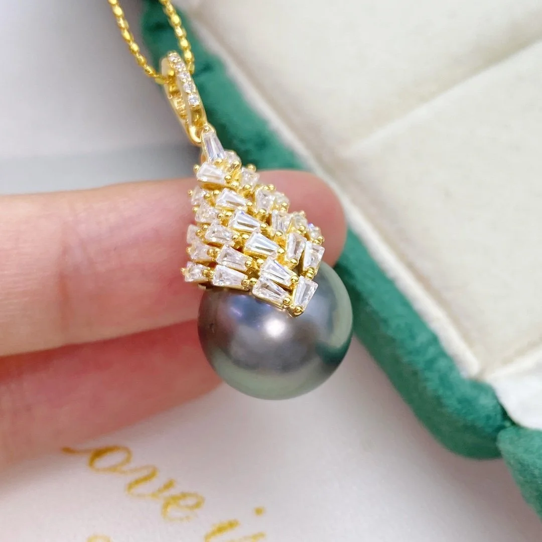 A close-up of a gold necklace with a large black pearl pendant, decorated with multiple small clear gemstones.