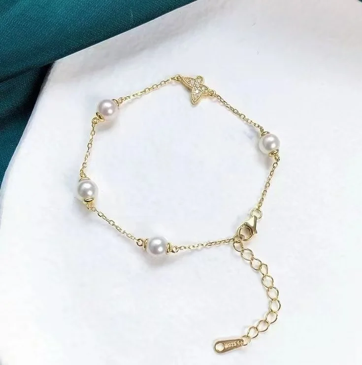 A gold chain bracelet with four white pearls and a small butterfly charm with sparkles, on a white background.