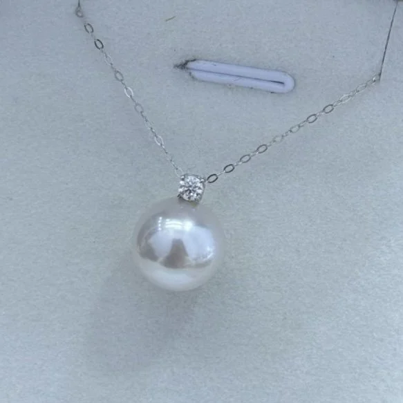 A pearl necklace with a rhinestone pendant displayed on a light-colored surface.