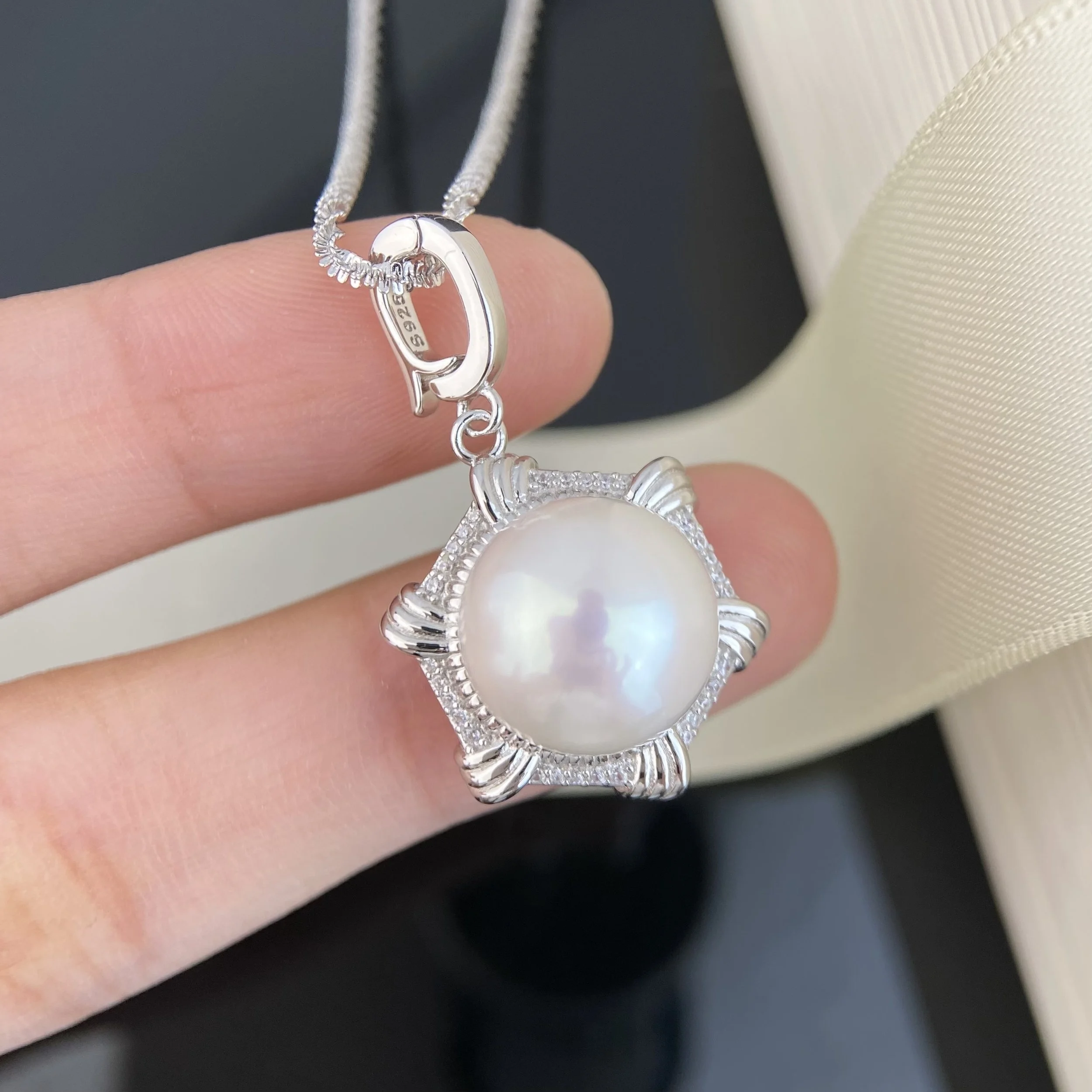 A silver necklace with a large white pearl pendant surrounded by a decorative silver frame.
