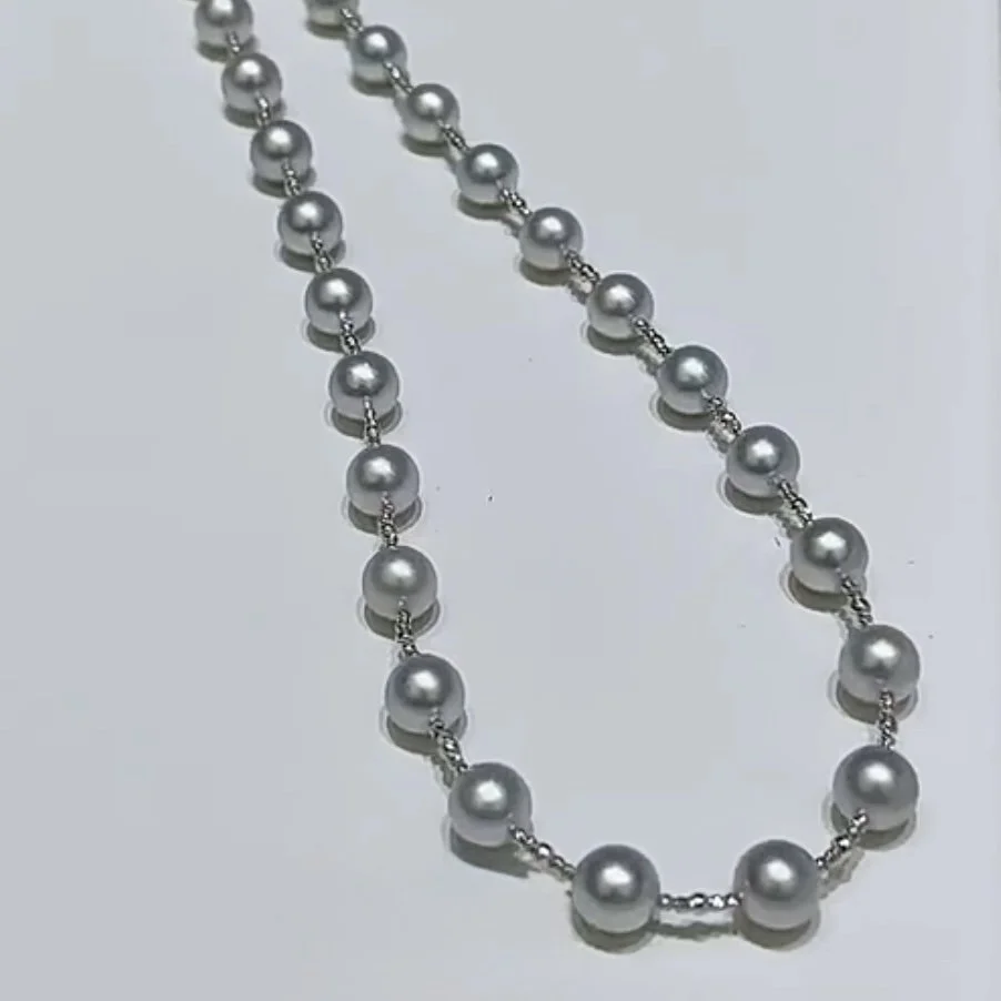 A silver pearl beaded necklace with small, shiny silver spacer beads on a light surface.
