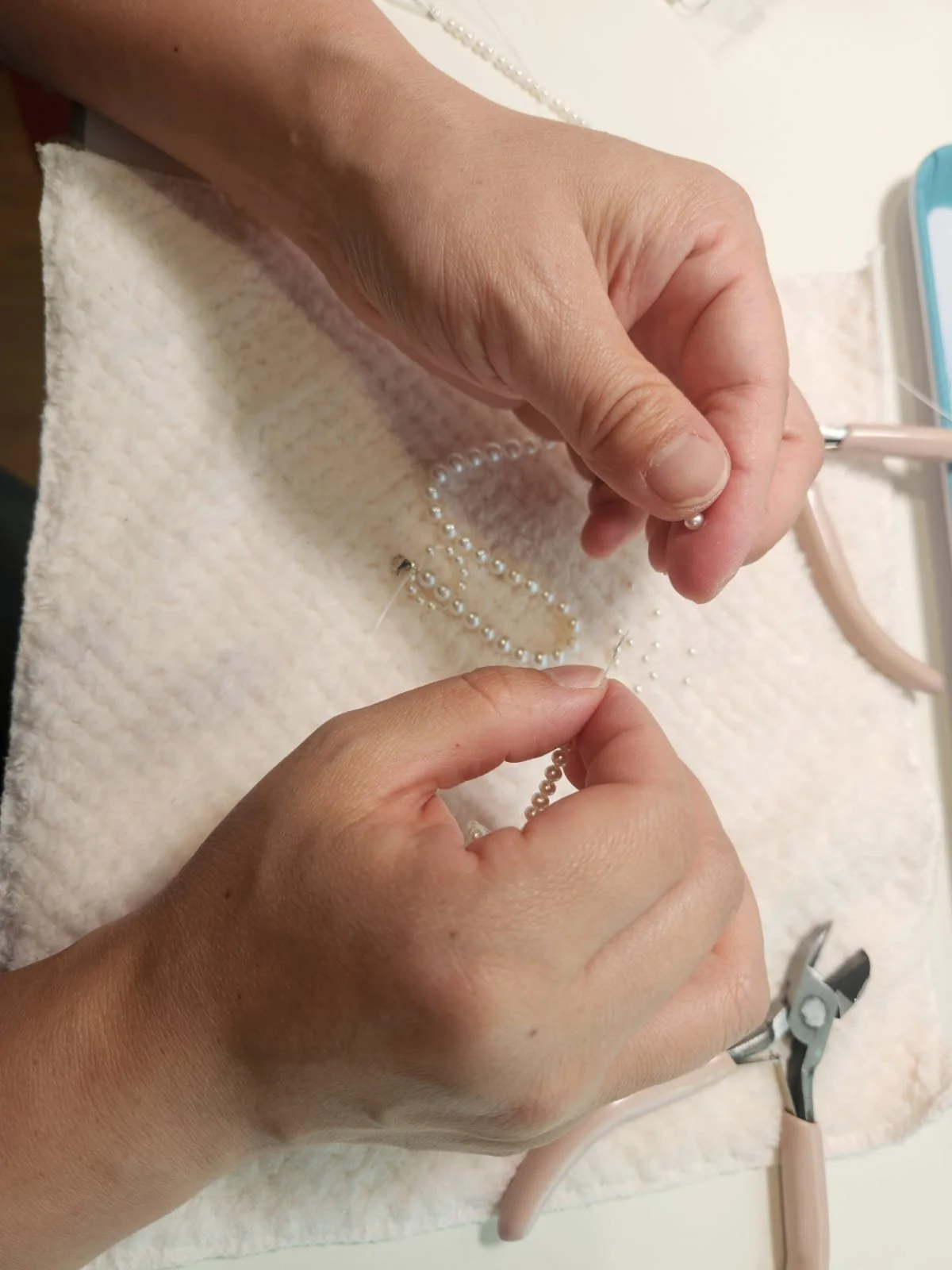 Craftman sewing a string of pearl beads with a needle and thread. Pearls and other jewelry-making tools are nearby.