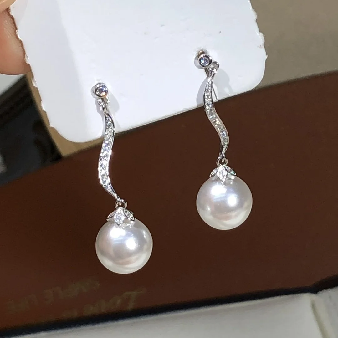 Pair of pearl drop earrings with curved silver hooks decorated with small gemstones, displayed on a white card.
