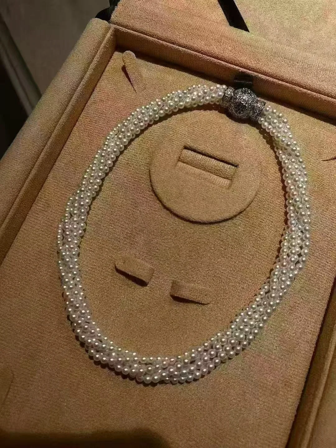 A pearl necklace with a decorative clasp, displayed in a beige jewelry box.