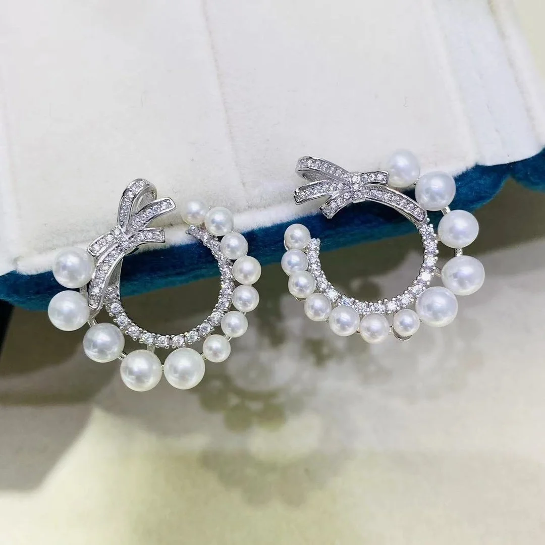 A pair of pearl and rhinestone earrings with bow-shaped tops, hanging from a cushioned display.