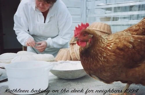 Kathleen Weber on a deck with a hen nearby, with a basket and a large bowl on the table.
