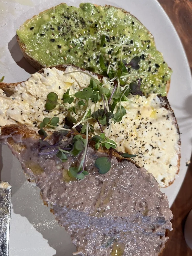 Della's Toast Trio. A plate with three slices of toast topped with different spreads and microgreens.