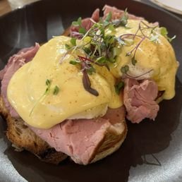 Eggs Benedict with ham, topped with hollandaise sauce and microgreens on an English muffin.