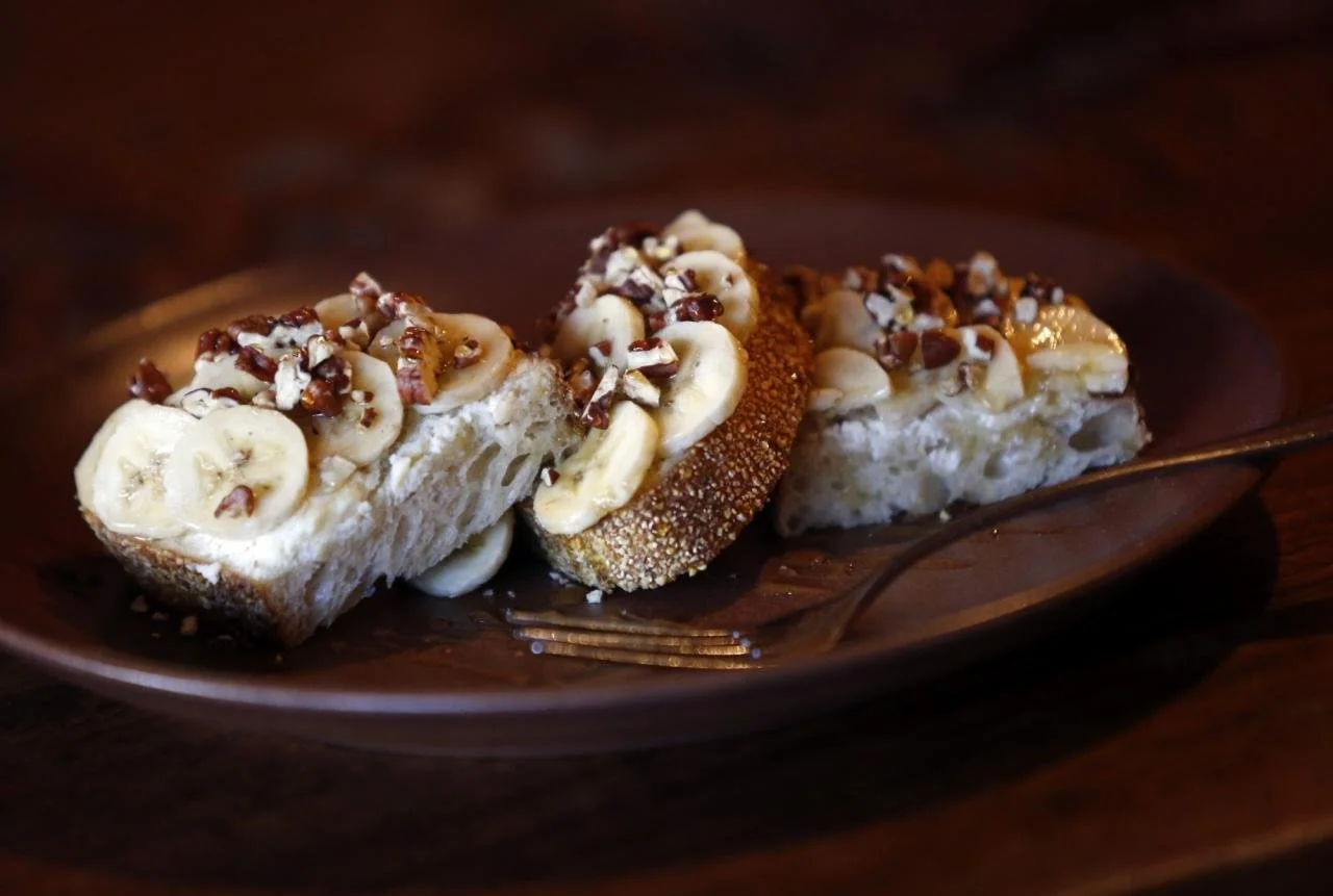 Slices of banana cream pie topped with chopped nuts on a brown plate with a fork.