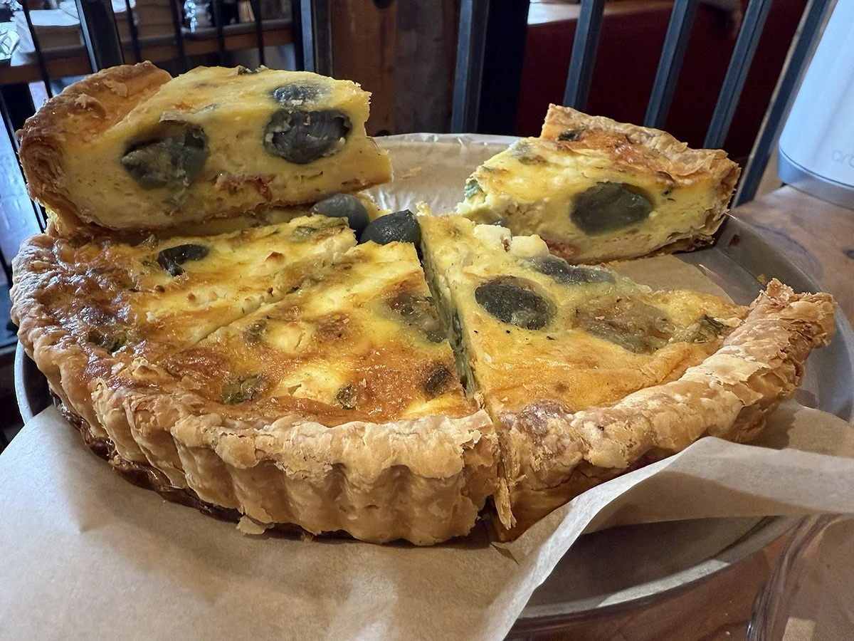 A cheese and olive quiche with a flaky crust on a plate.