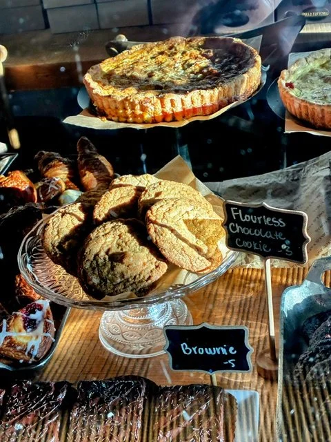 Assorted baked goods including cookies, a cheesecake, and brownies at a bakery display.