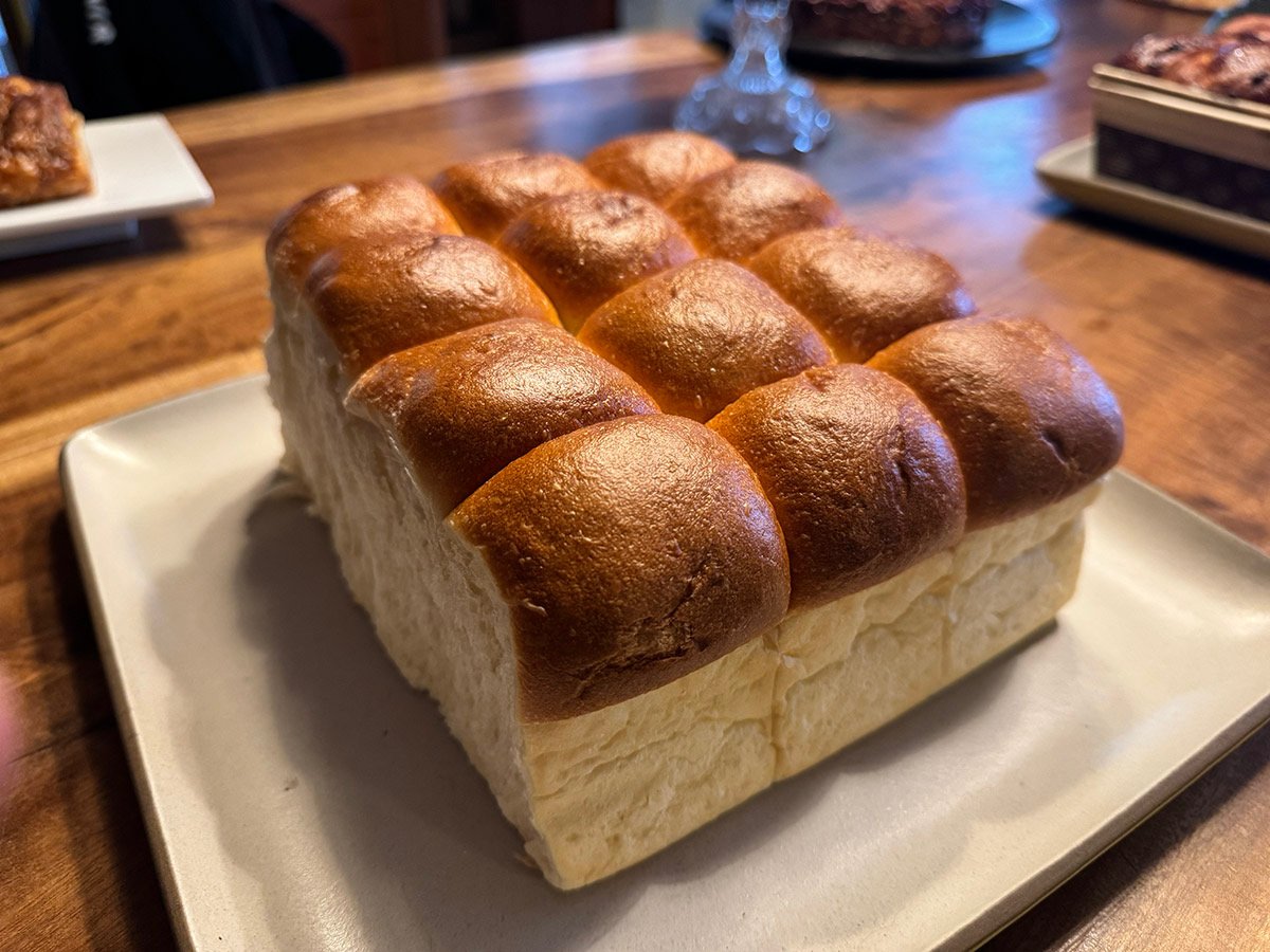 A tray of soft, golden-brown dinner rolls on a square white plate on a wooden table.