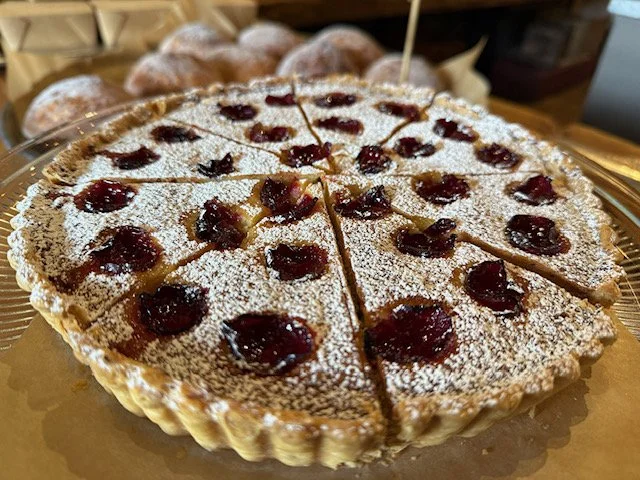 Cherry-topped pie dusted with powdered sugar on a gold tray, with muffins in the background.