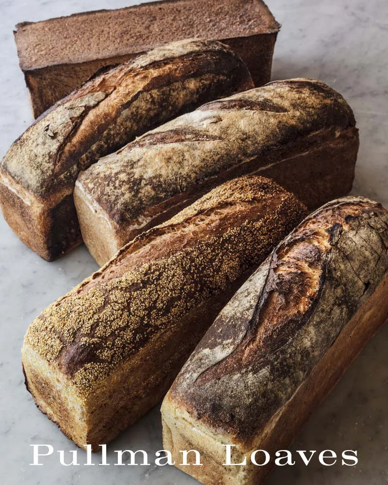 Five loaves of rustic bread on a marble surface with a wooden box in the background.