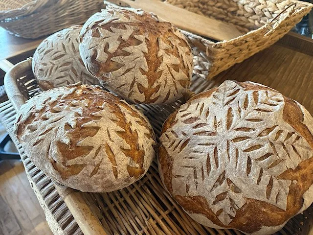 Three loaves of bread with leaf-shaped scoring on top, placed on a wicker tray.
