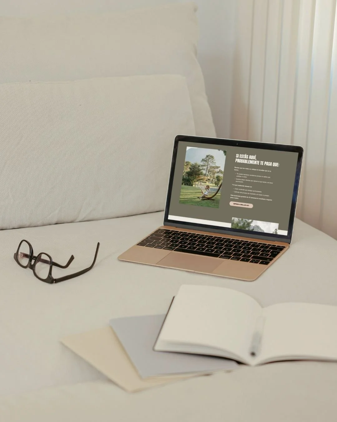 Un portátil en una cama, con unas gafas y un cuaderno abierto, y una pantalla que muestra una página con texto y una imagen de un parque.