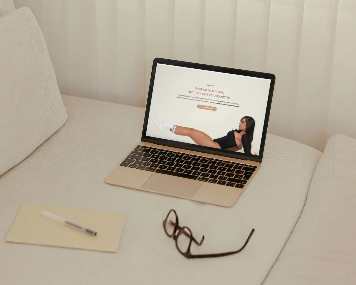 Portátil sobre sofá con gafas, cuaderno y bolígrafo, mostrando una página web de contacto con una mujer en la pantalla.