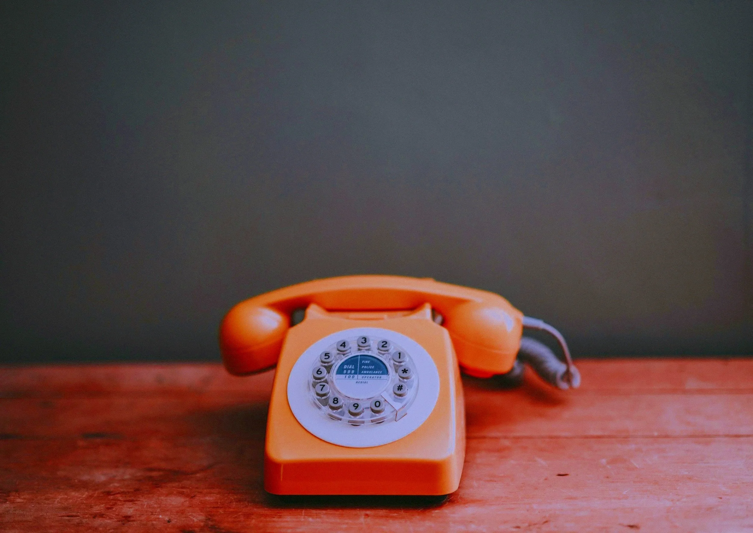 Orange rotary dial telephone on wooden surface with dark background.