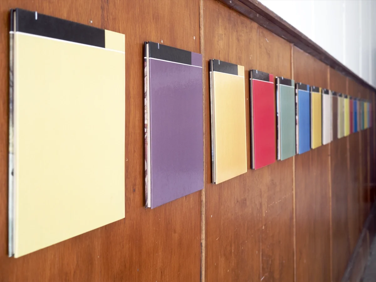 A row of colorful hardcover books on a wooden surface, arranged in order by artist Thomas Pendergast.
