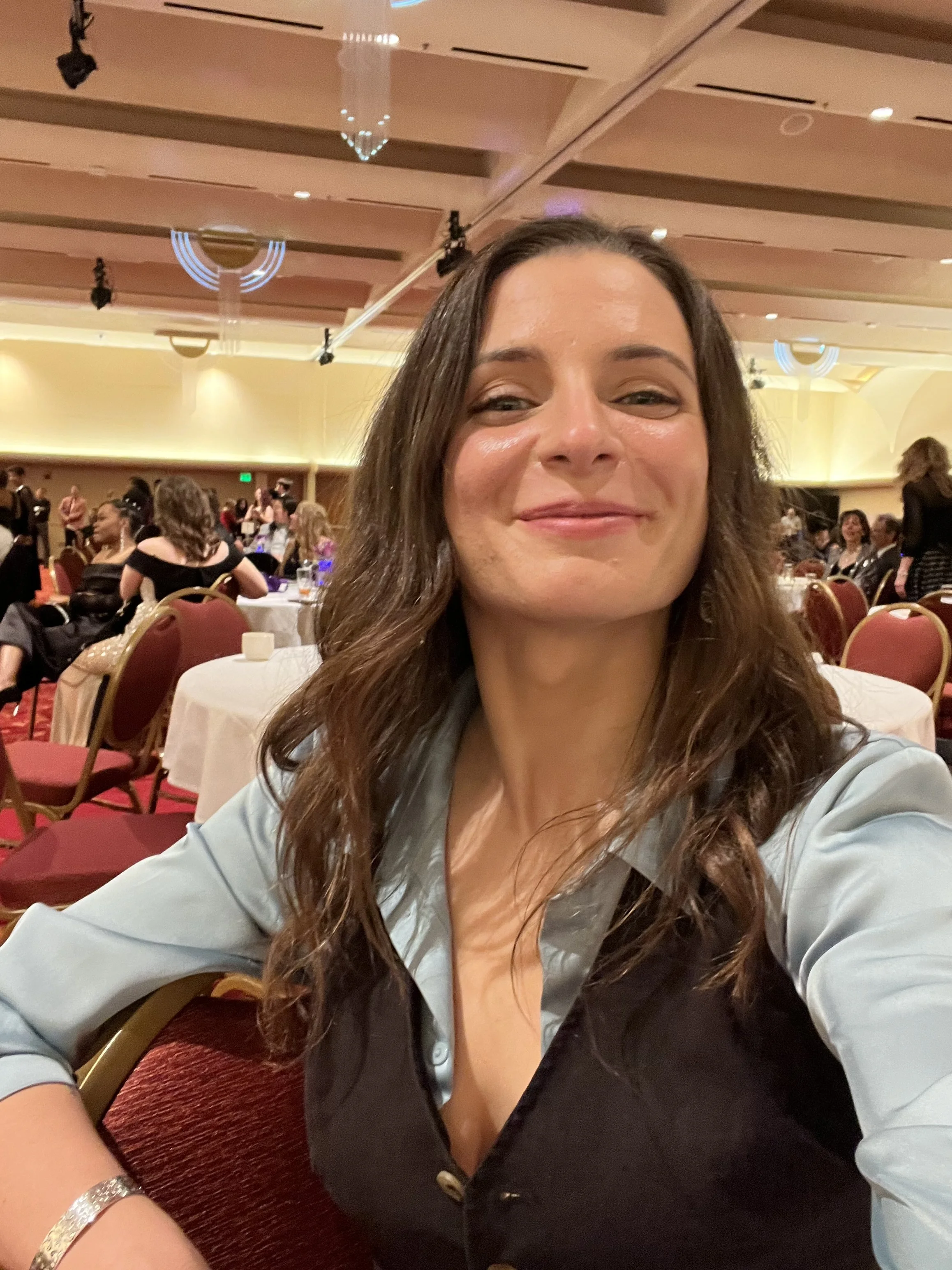 A Hygiene Ladies board member taking a selfie at a banquet hall with round tables and people in the background