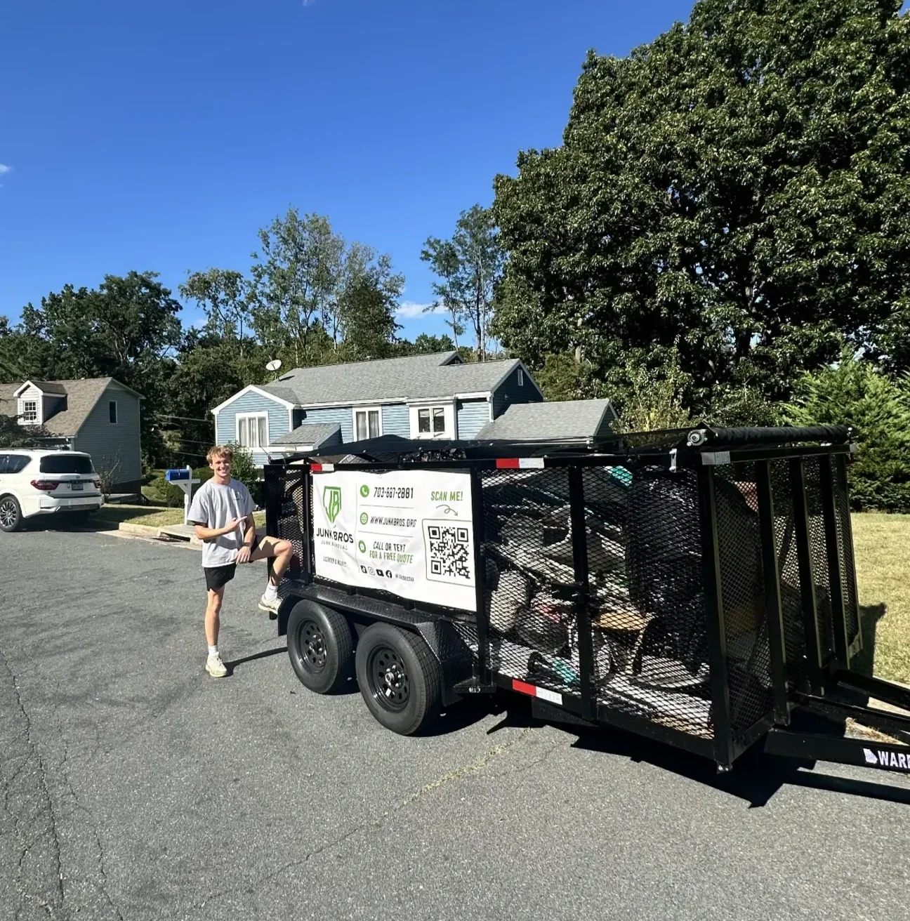 Junk Bros crew member next to a fully loaded junk removal trailer in a Virginia neighborhood