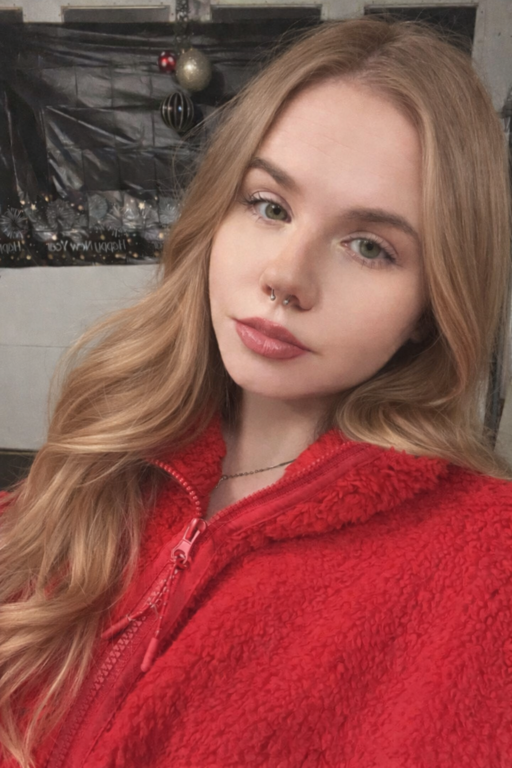 Close-up of young female with long sandy blonde hair, wearing a red fleece sweatshirt, and with a nose piercing 