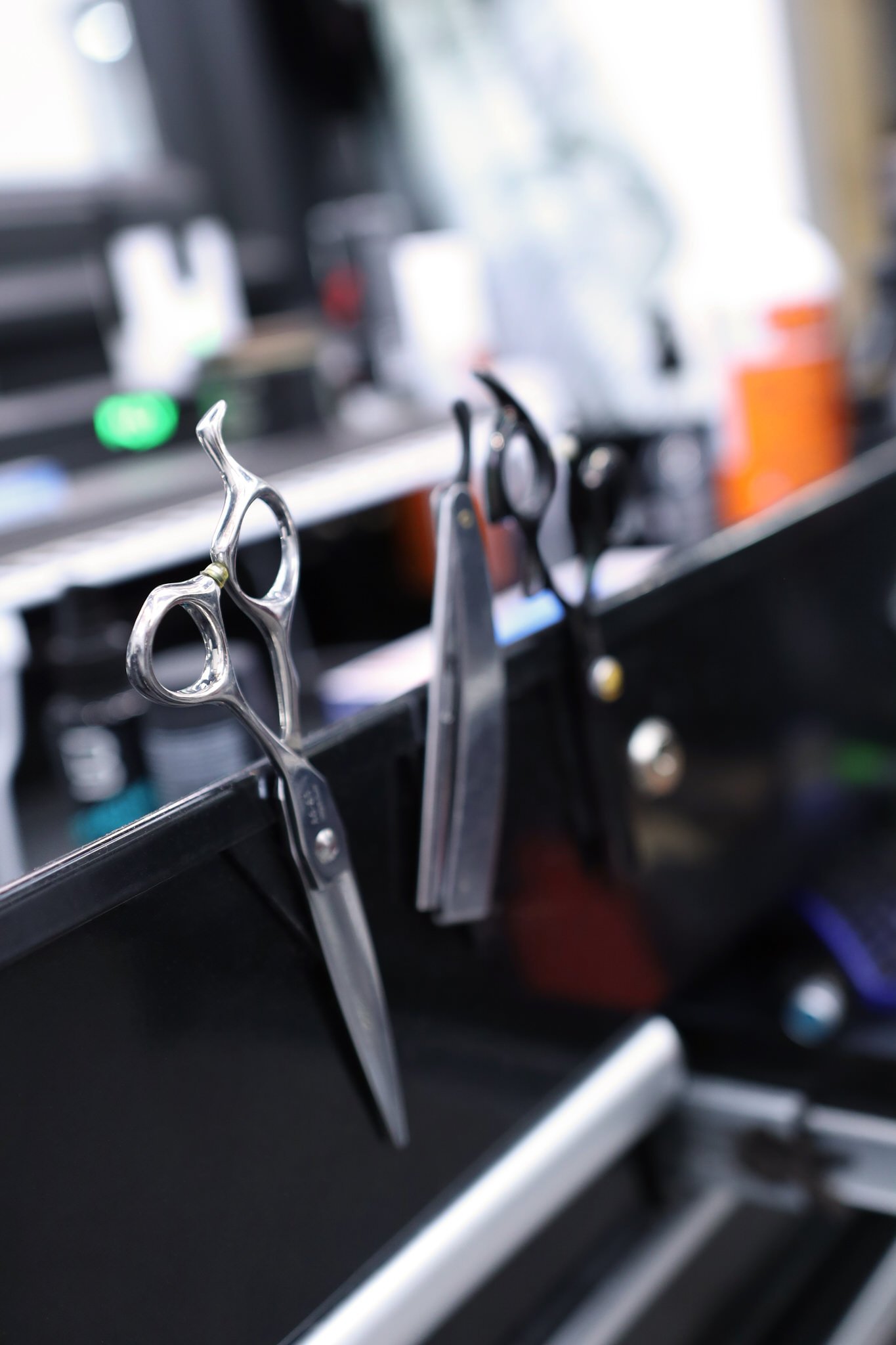 Shears and barbering tools attached magnetically to a black surface, with a very blurred background of a barbershop..