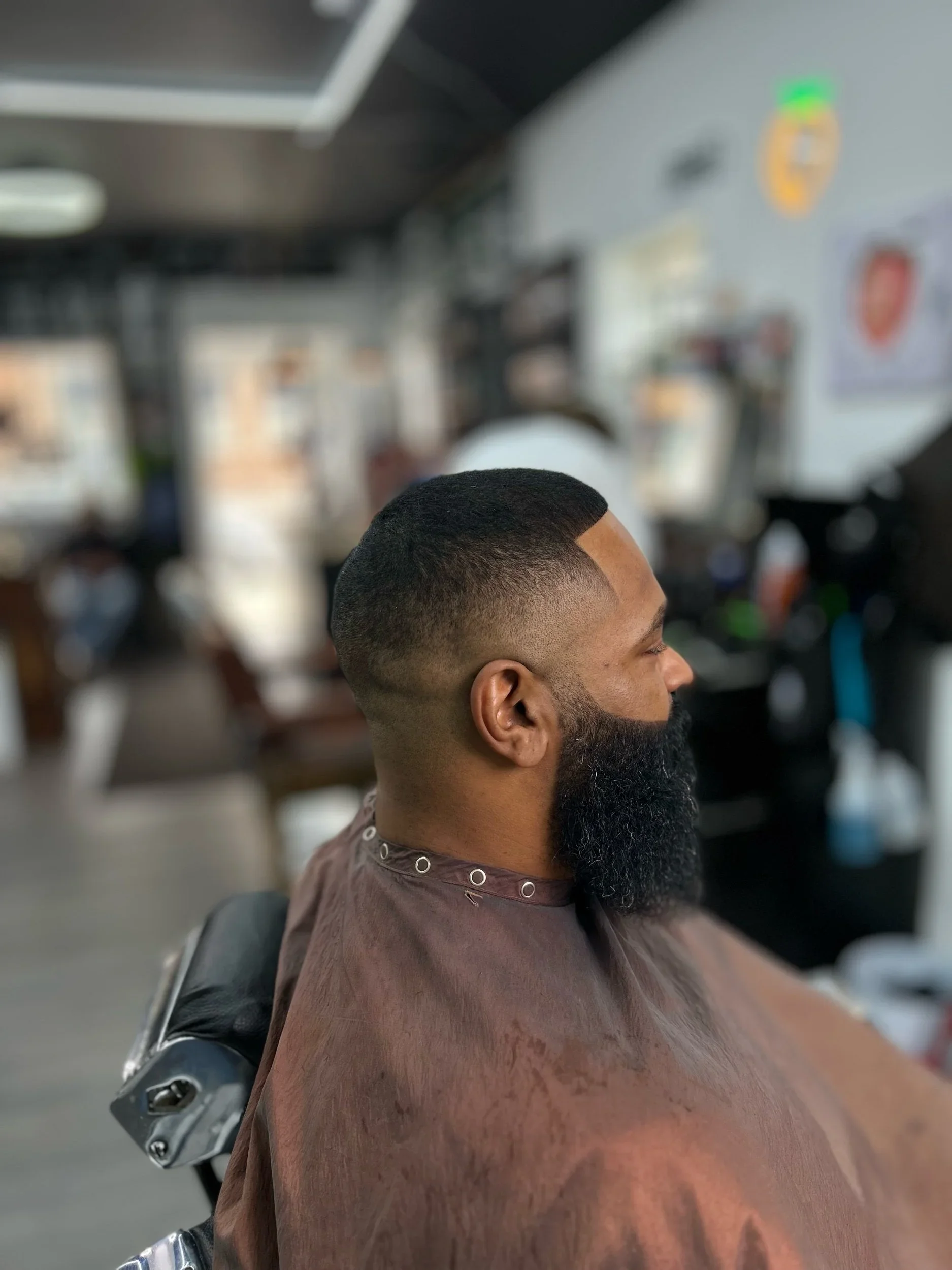 Side view of a man with a fresh haircut and full beard sitting in a barber shop.