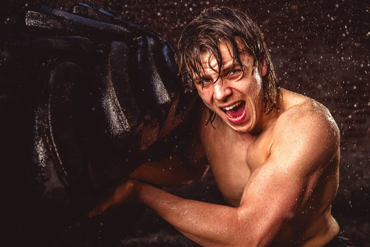 dramatic portrait of athlete lifting workout tire in the rain