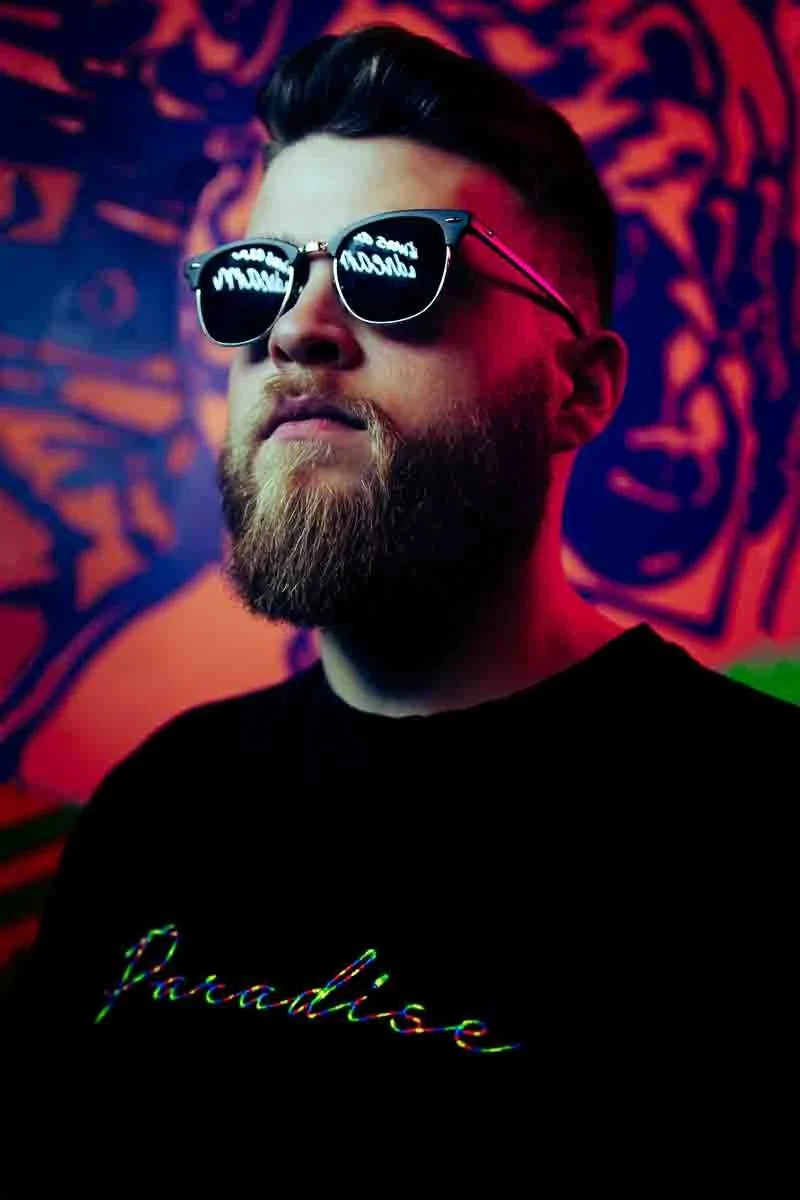 man posing with sunglasses in front of neon lights