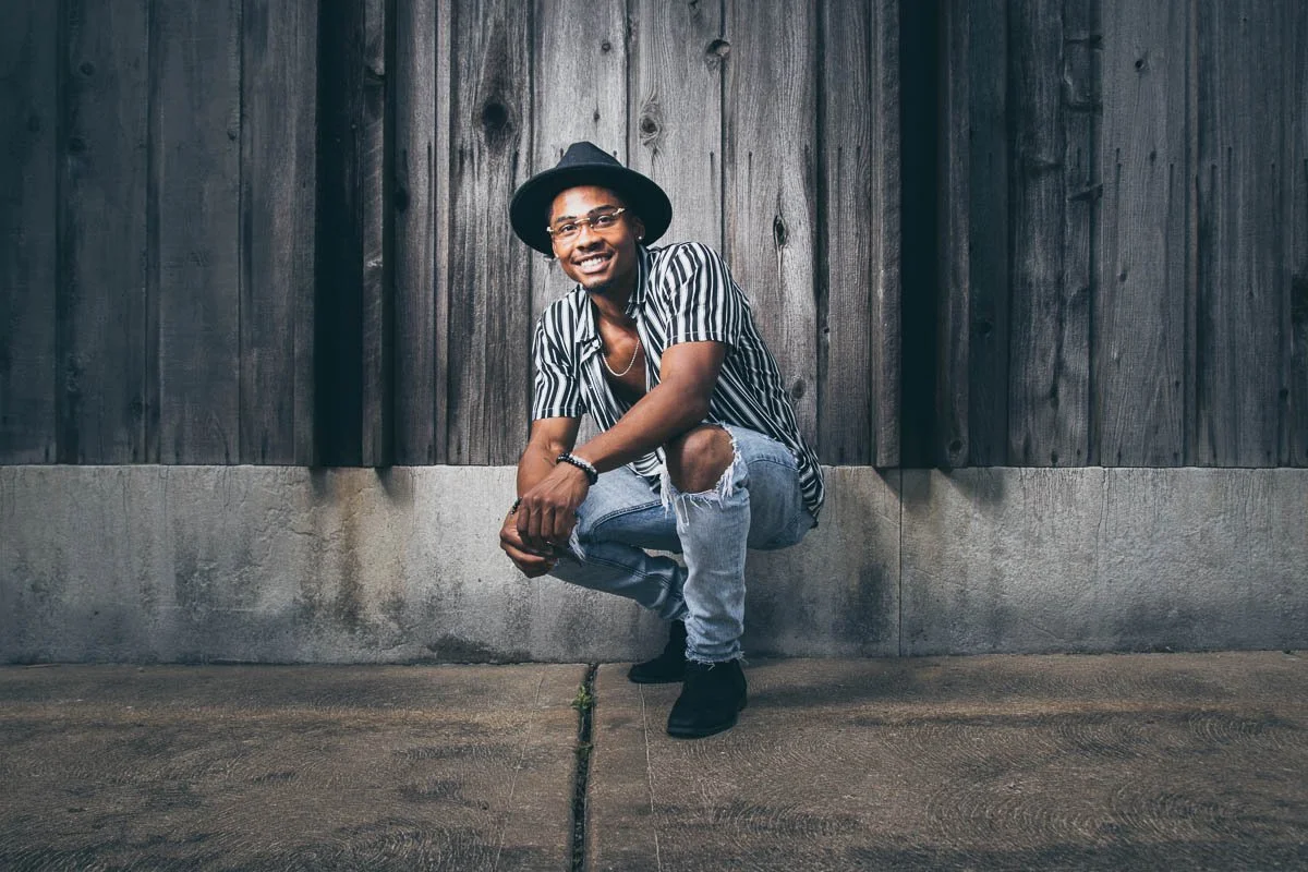 high school senior kneeling in front of wooden wall
